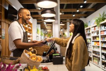 Happy customer smiling at the worker while paying with contactless credit card at a shopping terminal looking at each other